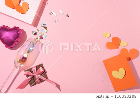 A chocolate bar, paper hearts, blank card, a heart balloon and a clear wine glass on a pink background. Empty space with a flat top-down view. A chocolate bar, paper hearts, blank card, a heart balloon and a clear wine glass on a pink background. Empty space with a flat top-down view. 110353288