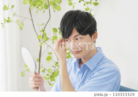 自宅で鏡でヘアスタイルを見る男性 110353329