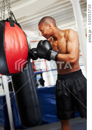 Black man, boxing and punching bag at gym for workout, exercise or self defense practice in fighting sport. African male person or boxer with gloves for indoor training or martial arts at health club Black man, boxing and punching bag at gym for workout, exercise or self defense practice in fighting sport. African male person or boxer with gloves for indoor training or martial arts at health club 110353710