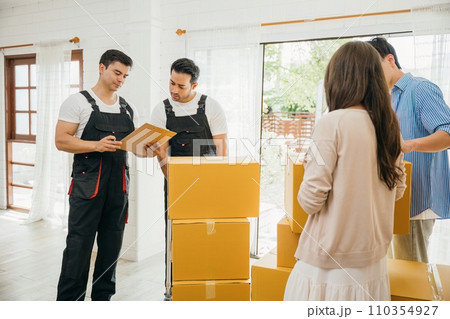 Couple checks moving checklist worker holds cardboard box. Professional movers ensure smooth relocation service. Teamwork and efficient home moving displayed. Movind Day 110354927