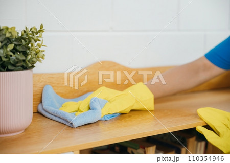 A cheerful housewife in yellow gloves diligently cleans the table. Her commitment to home hygiene and cleanliness reflects in her routine cleaning tasks. The woman is. A cheerful housewife in yellow gloves diligently cleans the table. Her commitment to home hygiene and cleanliness reflects in her routine cleaning tasks. The woman is. 110354946