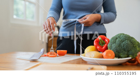 Young woman asian measure her waist in the kitchen the with vegetables and fruits. Concept of healthy eating and dieting 110355195