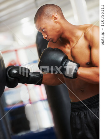 Boxing, gloves and black man training in gym with fitness, power and workout challenge. Strong body, muscle and boxer in club, athlete fighting with bag for exercise and confidence in competition. 110356111