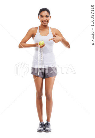 Woman, lose weight and pointing to measuring tape and apple in white background or studio. Indian, model and happy with results of fitness, wellness and diet with healthy food, nutrition and fruit 110357110
