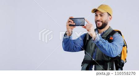 Hiking, backpack and happy man with phone in studio for video call, photography or memory on grey background. Travel, smartphone and male backpacker with app for live streaming journey in nature 110358270