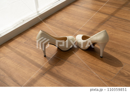 Beige high heels on wooden floor radiating bridal elegance for the chic wedding ceremony. Sophisticated and glossy wedding stilettos basking in sunlight before the marriage celebration 110359851