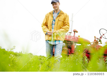 Its just me and my tractor. Portrait of a farmer standing in a field with his tractor parked behind him - Copyspace. 110360003