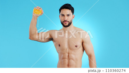 Orange, splash and portrait of man in studio for vitamin C, natural cosmetics or healthy diet on blue background. Fruit, squeeze or model face with citrus, juice or skin detox, wellness or nutrition 110360274