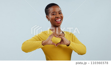 Happy black woman, portrait and heart hands for love, care or romance against a gray studio background. Face of African female person or model showing like emoji, shape or romantic gesture on mockup 110360378
