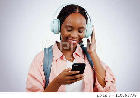Woman, student and headphones on mobile for music, elearning audio and education on a white background. Happy african person in backpack and electronics for listening or streaming on phone in studio 110361738