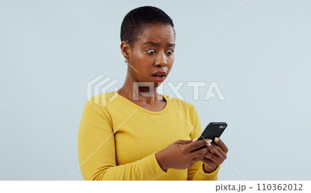 Black woman, phone and shocking news on social media, terrifying or online against a studio background. Face of surprised African female person or model on mobile smartphone for alert notification 110362012