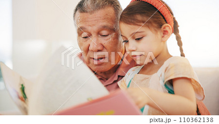 Grandparent, kid and reading book with smile, home and child development, grandchild and couch. Man, lounge or bonding together for relationship, family and retired with girl, house and happy 110362138