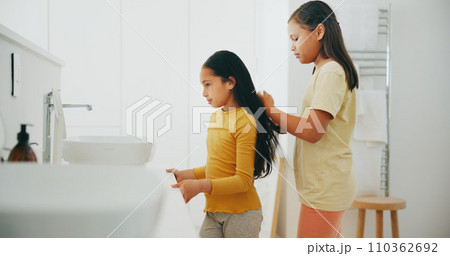 Family, bathroom and a girl brushing the hair of her sister in their home for morning routine or care. Kids, beauty or haircare with a young female child and sibling in their apartment for hygiene Family, bathroom and a girl brushing the hair of her sister in their home for morning routine or care. Kids, beauty or haircare with a young female child and sibling in their apartment for hygiene 110362692