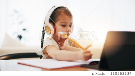 Girl, headphones and writing in book for elearning, education or study on desk at home. Female person, little child or kid taking notes with tablet, headset or technology for virtual class at house 110363134