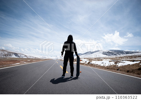 Skateboarder skateboarding on snowy country road 110363522