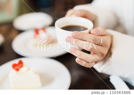 Woman hand holding hot Coffee Cup with Cheese Cake. Dessert and beverage in winter day Woman hand holding hot Coffee Cup with Cheese Cake. Dessert and beverage in winter day 110363866