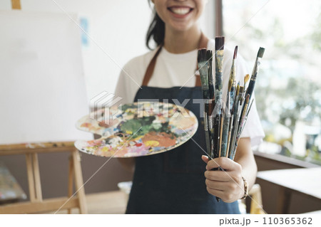 A close-up of the artist hands wearing an apron smeared with paint. Clutching many brushes and paintbrushes. A close-up of the artist hands wearing an apron smeared with paint. Clutching many brushes and paintbrushes. 110365362
