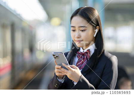 スマートホンの画面を見るイヤホンをつけた女子高校生　電車通学　イメージ 110365693