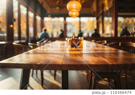 Empty wooden table top with restaurant full of guests in background with bokeh autumn sunlight. 110366474