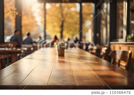 Empty wooden table top with restaurant full of guests in background with bokeh autumn sunlight. 110366478