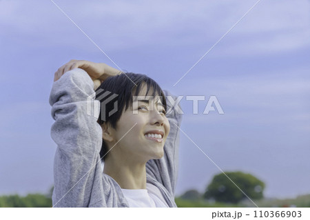 土手で青空を見上げる若い女性 110366903