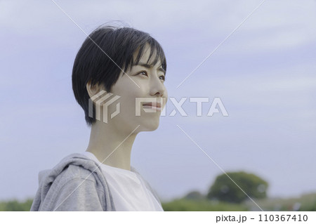 土手で青空を見上げる若い女性 110367410