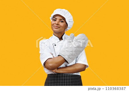 Confident black female chef with crossed arms wearing an oven mitt Confident black female chef with crossed arms wearing an oven mitt 110368387
