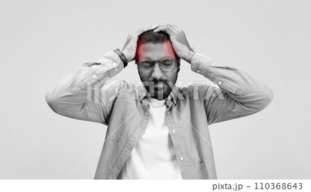 A stressed man in a casual linen shirt and glasses grasps his head in frustration or headache 110368643