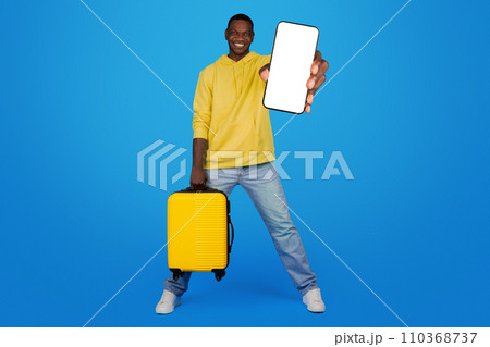 An exuberant Black man strides forward with a yellow suitcase, holding up a smartphone with a mockup screen An exuberant Black man strides forward with a yellow suitcase, holding up a smartphone with a mockup screen 110368737