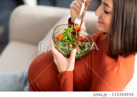 Pregnant lady eating vegetable salad resting on sofa at home Pregnant lady eating vegetable salad resting on sofa at home 110368938