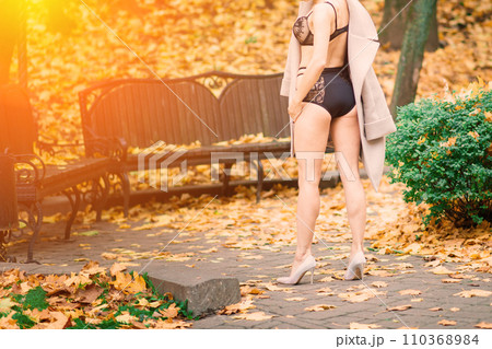 Gorgeous brunette female in bodysuit, lingerie and coat walking in park 110368984