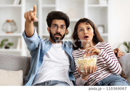Shocked Young Indian Couple Watching Horror Movie On TV 110369067