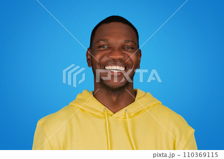 An African man in a yellow hoodie beams with a radiant smile, showcasing white teeth 110369115