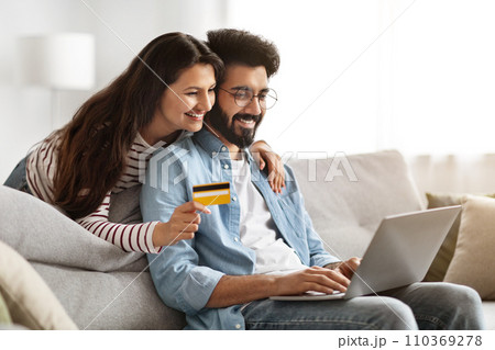 Happy indian couple using laptop and credit card at home Happy indian couple using laptop and credit card at home 110369278