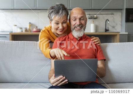 Smiling Senior Spouses With Laptop Shopping Online Together At Home Smiling Senior Spouses With Laptop Shopping Online Together At Home 110369317