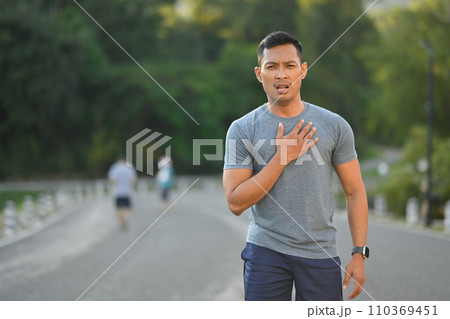 Tired sportsman touching his chest feeling pain in heart during exercise outdoor 110369451