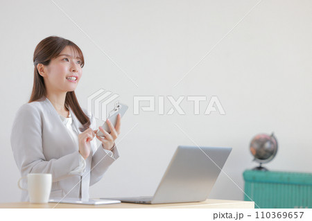 スマホを操作しながら斜め上を見るビジネスウーマン1 110369657