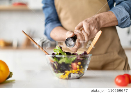 Focused elderly chef preparing nutritious vegetable salad, adding spices for flavor 110369677