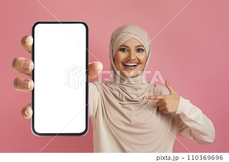 Cheerful Arab Lady In Hijab Pointing At Smartphone With White Blank Screen 110369696