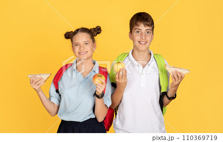 Smiling young schoolchildren with colorful backpacks holding apples and sandwiches Smiling young schoolchildren with colorful backpacks holding apples and sandwiches 110369719