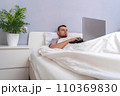 A man with laptop is lying in bed. Freelancer 110369830