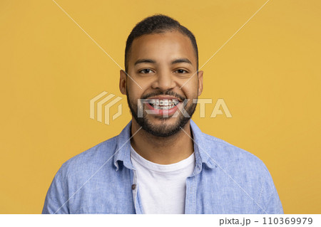 Cheerful young black man with dental braces posing against yellow background Cheerful young black man with dental braces posing against yellow background 110369979