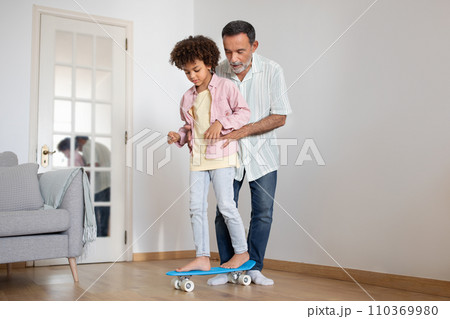 Mature Grandpa Teaching His Grandchild To Ride Skateboard At Home 110369980