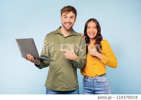 Couple with laptop pointing at computer on blue background 110370019