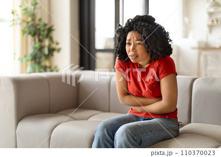 Worried young black woman sitting arms crossed and looking troubled 110370023
