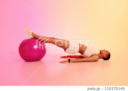 A woman with a shaved head relaxes in a supine position, legs raised on a pink exercise ball A woman with a shaved head relaxes in a supine position, legs raised on a pink exercise ball 110370140