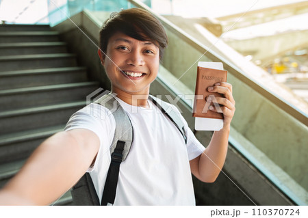 Cheerful asian man taking selfie, showing passport and tickets Cheerful asian man taking selfie, showing passport and tickets 110370724