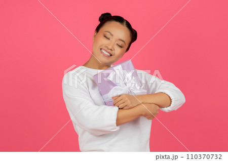 Smiling Young Asian Lady Hugging Wrapped Gift Box Smiling Young Asian Lady Hugging Wrapped Gift Box 110370732