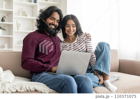 Positive young indian couple watching movie on laptop at home Positive young indian couple watching movie on laptop at home 110371075