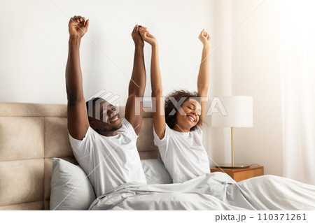 Rested black young couple waking up in bedroom stretching arms Rested black young couple waking up in bedroom stretching arms 110371261